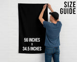 A man is hanging a black banner on a white wall, with the banner displaying the size guide for 56 inches by 34.5 inches.