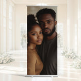 A man and a woman are standing close together, with the woman appearing to be looking at the man. The background features a white interior with floral decorations.